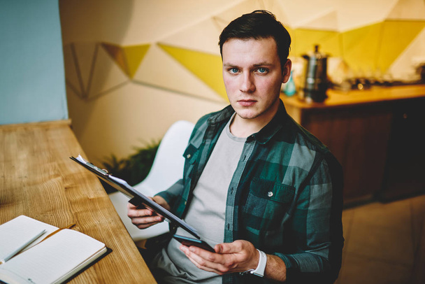 Portrait of young casually dressed male learning information for college exams holding folder,serious male looking at camera making planning for startup checking documents in coworking space - Фото, зображення