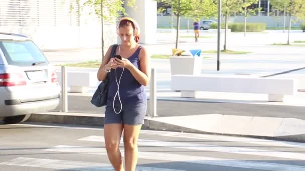 Lachende vrouw luister muziek tijdens het oversteken van de weg op het zebrapad  - Video