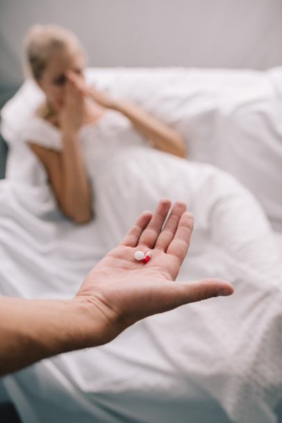 обрезанный снимок мужчины с таблетками в руке и беременная женщина чувствует дискомфорт дома
 - Фото, изображение