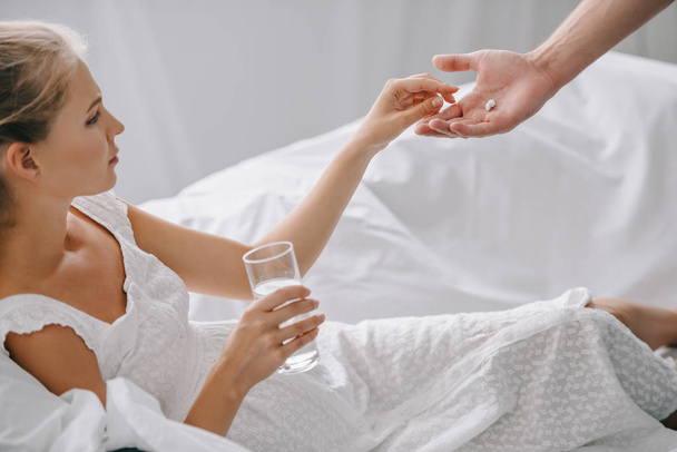 częściowy widok człowieka podawaniem leków w ciąży kobieta w białych nightie na kanapie w domu - Zdjęcie, obraz