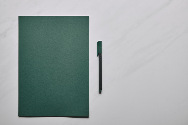 Green paper and pen on white marble background - Photo, image