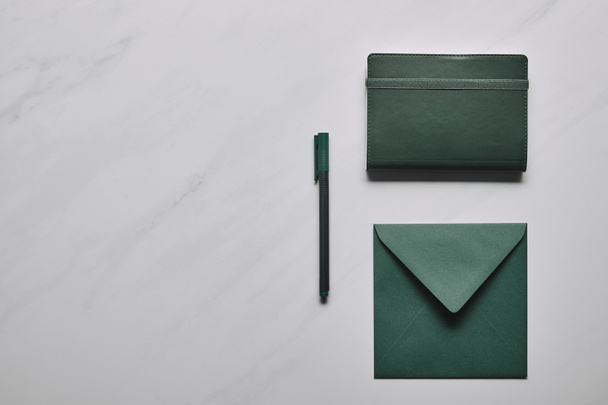 Green envelope and notebook with pen on white marble background - Foto, Bild
