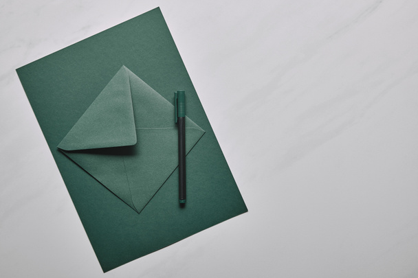 Green envelope with pen on white marble background - Photo, Image