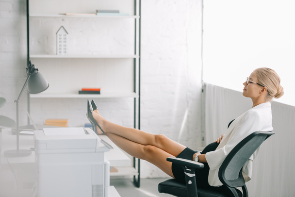 side view of pregnant businesswoman resting with legs on table at workplace in office - Foto, afbeelding