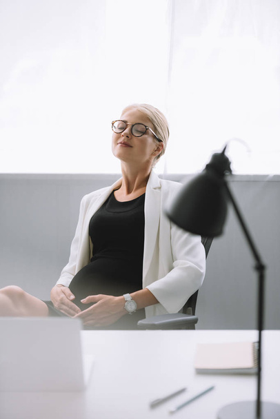 portrait of pregnant businesswoman in eyeglasses at workplace in office - Фото, зображення