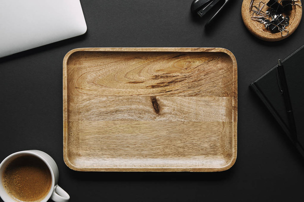Empty wooden board on black background with laptop and stationery - 写真・画像