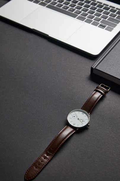 Brązowy zegarek przez otwarty laptop na czarnym tle - Zdjęcie, obraz