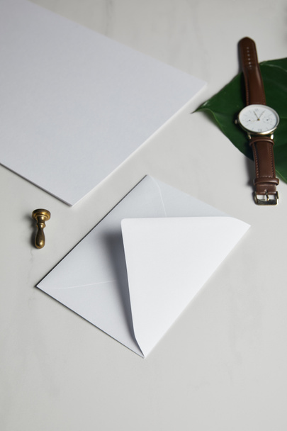 White envelope with brown watch on white marble background - 写真・画像