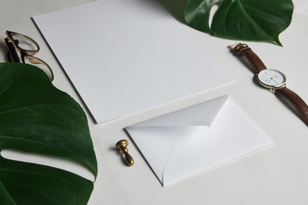 Business mock up set with envelope and watch on white marble background with monstera leaves - Fotografie, Obrázek
