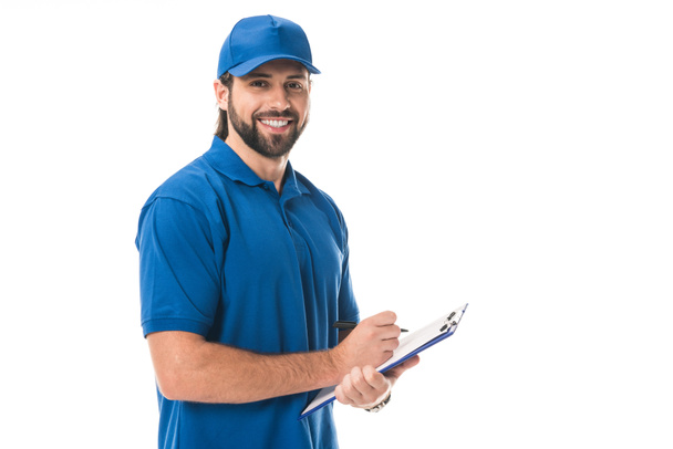 happy young delivery man writing on clipboard and smiling at camera isolated on white - Photo, Image