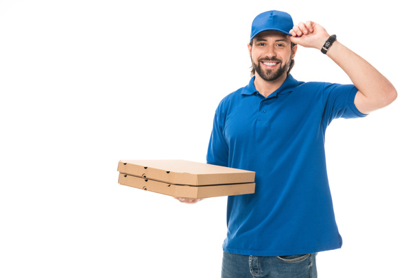 happy delivery man holding boxes with pizza adjusting cap, smiling at camera isolated on white - Photo, Image