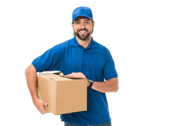 όμορφος νεαρού delivery άνδρας κρατώντας κουτί από χαρτόνι και να χαμογελά στη φωτογραφική μηχανή που απομονώνονται σε λευκό - Φωτογραφία, εικόνα
