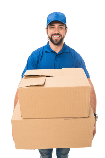 handsome happy young delivery man holding cardboard boxes and smiling at camera isolated on white - Foto, Imagem