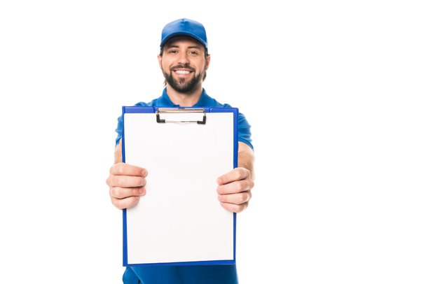 handsome young delivery man holding blank clipboard and smiling at camera isolated on white - Foto, immagini