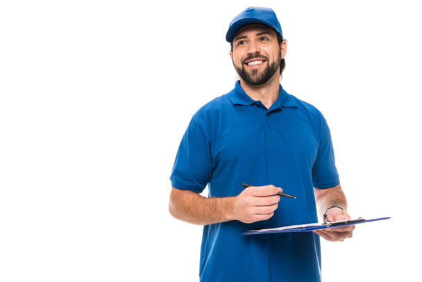 handsome happy delivery man writing on clipboard and looking away isolated on white - Photo, Image