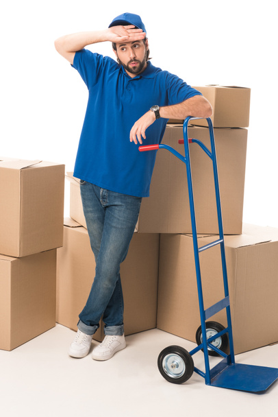 tired delivery man standing between cardboard boxes isolated on white  - Fotó, kép