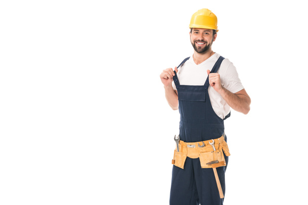 handsome happy workman in tool belt and hard hat smiling at camera isolated on white  - Фото, изображение