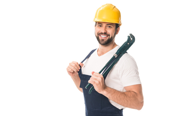 schöner glücklicher Arbeiter, der einen verstellbaren Schraubenschlüssel in der Hand hält und isoliert auf weiß in die Kamera lächelt  - Foto, Bild