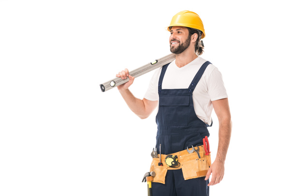 happy handsome workman holding level tool and looking away isolated on white - Φωτογραφία, εικόνα