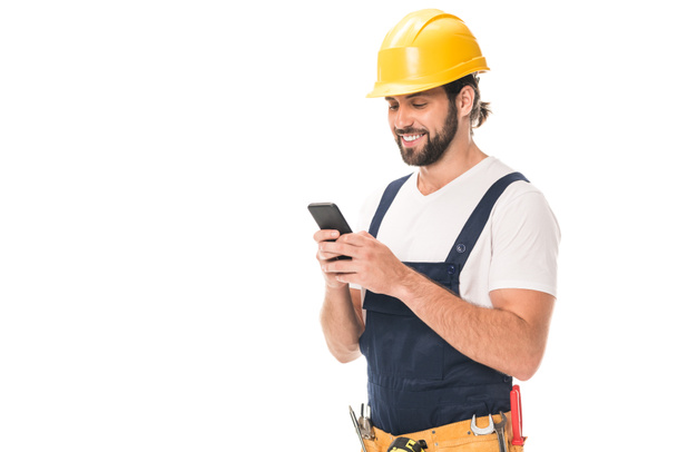 trabajador feliz en sombrero duro utilizando teléfono inteligente aislado en blanco
 - Foto, Imagen