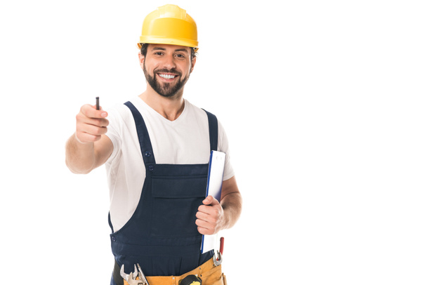 handsome construction worker in hard hat holding clipboard and smiling at camera isolated on white - Fotoğraf, Görsel