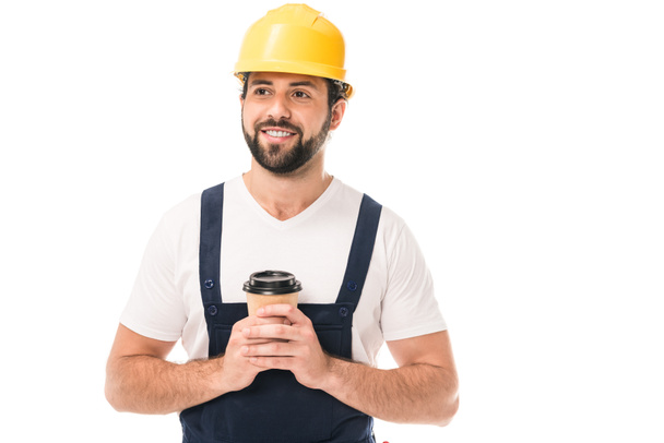handsome smiling workman in hard hat holding coffee to go and looking away isolated on white - Photo, Image