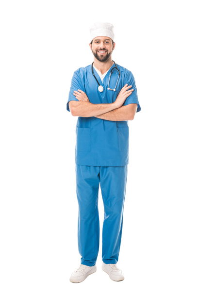full length view of bearded surgeon standing with crossed arms and smiling at camera isolated on white  - Foto, imagen