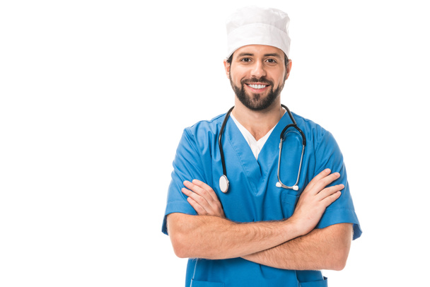 bonito barbudo cirurgião de pé com cruzados braços e sorrindo para câmera isolado no branco
  - Foto, Imagem