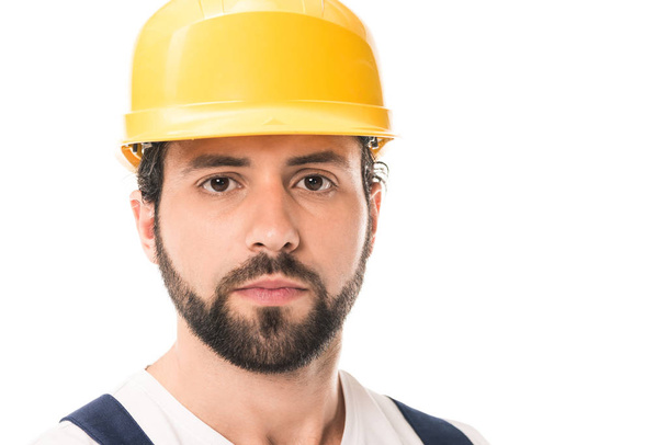 vista de cerca del trabajador guapo en sombrero duro mirando a la cámara aislada en blanco
 - Foto, Imagen