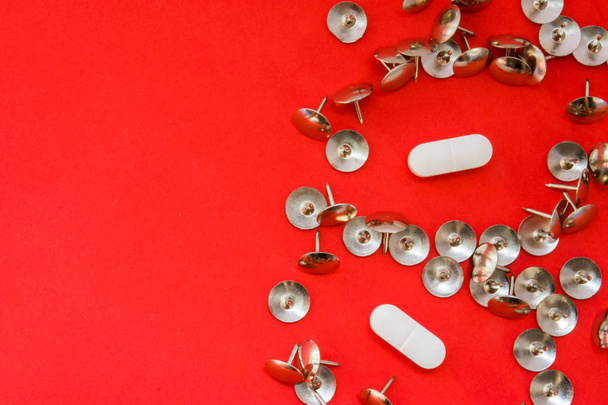 White pills surrounded by sharp thumbtacks at distance from them is on red background with empty area for headers top view. Concept images illustrating effect of painkillers and struggle with pain - Photo, Image