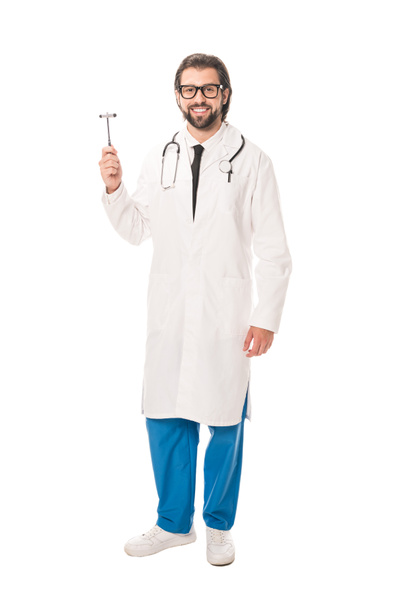 Προβολή πλήρους μήκους του γιατρού κρατώντας ΝΕΥΡΟΛΟΓΙΚΑ σφυρια και να χαμογελά στη φωτογραφική μηχανή που απομονώνονται σε λευκό - Φωτογραφία, εικόνα
