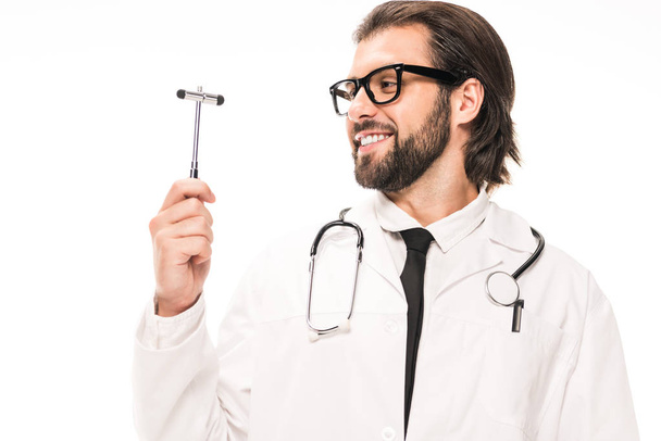 smiling doctor in white coat and eyeglasses holding reflex hammer isolated on white - Foto, Imagen