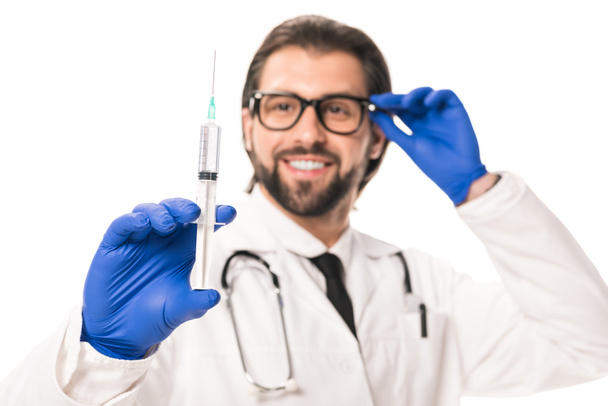 zbliżenie uśmiechający się lekarza w Rękawice medyczne, trzymając strzykawkę na białym tle - Zdjęcie, obraz