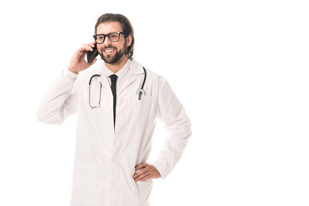 happy doctor in eyeglasses and white coat talking by smartphone isolated on white - Fotó, kép