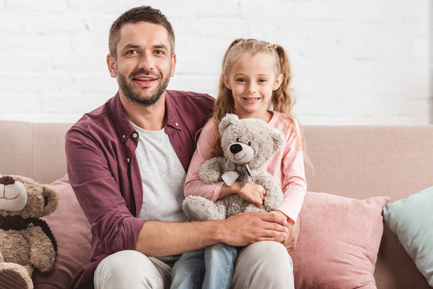 daughter holding teddy bear on father knees and looking at camera - Fotoğraf, Görsel