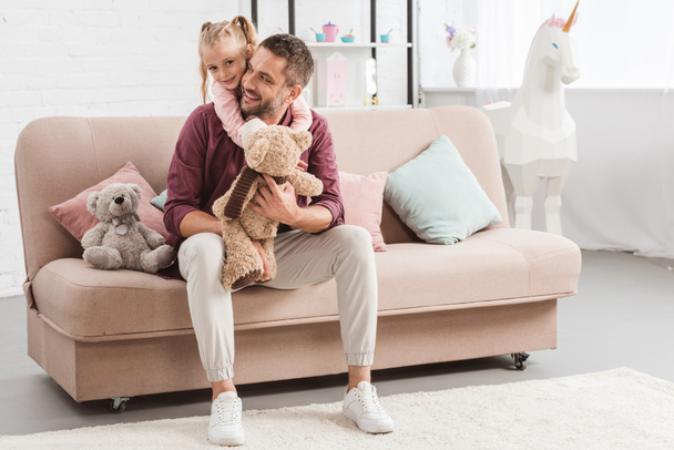 daughter hugging father on sofa with toys at home - Photo, Image