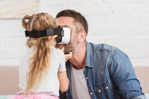 father and smiling daughter using virtual reality headset together at home - Photo, Image