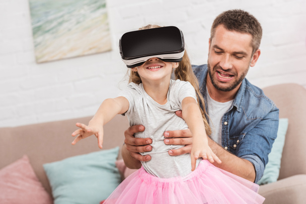 father and daughter having fun and using virtual reality headset on sofa - Fotó, kép
