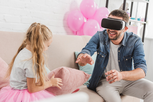 cheerful dad and daughter having fun and using virtual reality headset on sofa - Фото, зображення