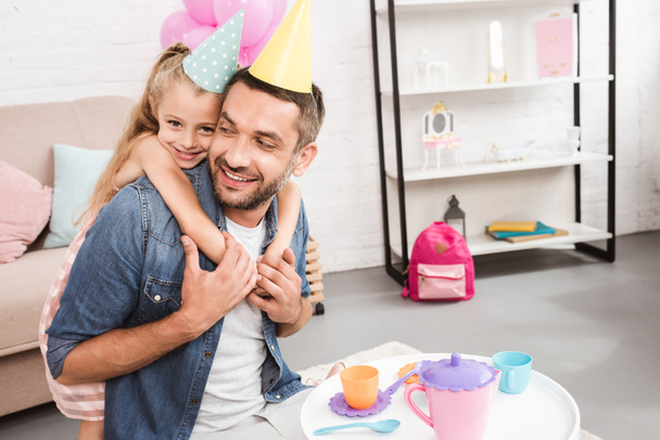father and daughter in cone hats playing tea party at home - Photo, Image