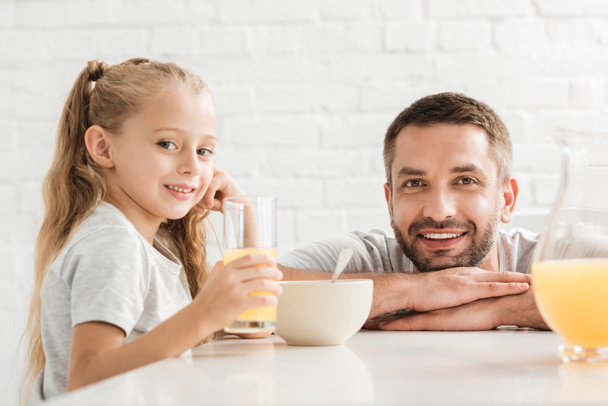 father and daughter drinking orange juice and looking at camera - Photo, Image