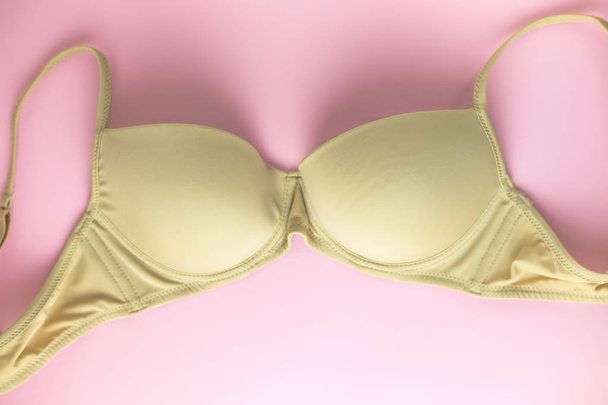Beige bra on pink background as symbol of female breast disease. Breast cancer awareness month. Minimalistic style. Top view. Flat lay. - Foto, imagen