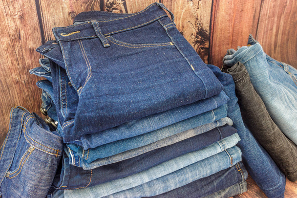 Various shades of jeans stacked on a wooden background, close up - Photo, Image