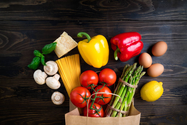 Healthy food background. Healthy food in paper bag vegetables, pasta, eggs, cheese and mushrooms on dark. Ingredients for cooking pasta. Shopping food supermarket concept. Top view - Photo, Image