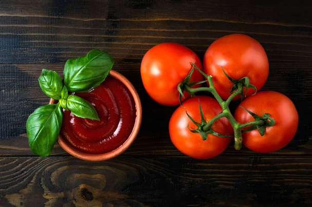 Molho de ketchup de tomate em uma tigela com manjericão e tomates na mesa de madeira escura. Vista superior
 - Foto, Imagem