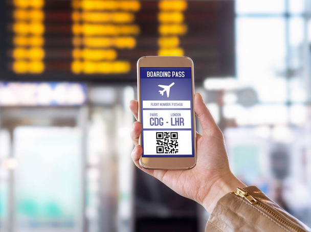 Boarding pass in mobile phone. Woman holding smartphone in airport with modern ticket on screen. Easy and fast access to aeroplane. Terminal and timetable in the blurred background. - Photo, Image
