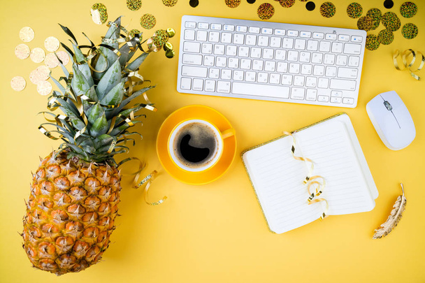Fashion feminine home office, workspace flat lay. Pineapple, coffee cup, golden confetti, women's accessories and notebook on yellow table. Festive female background.  Top view - Photo, Image