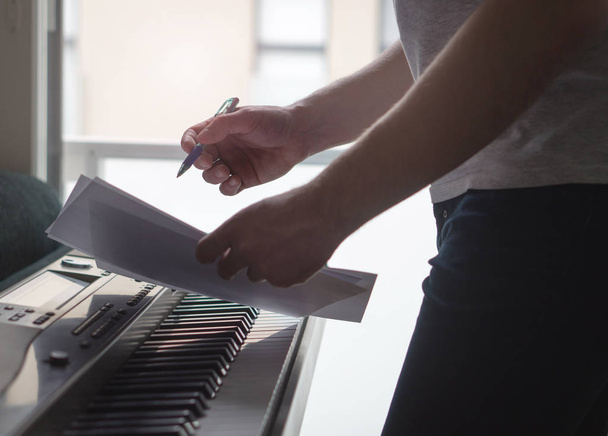 Musician brainstorming and innovating new song ideas at piano by the window. Composer writing notes to paper or planning arrangement. Man come up with pop lyrics. Inspiration and creativity concept. - Photo, image