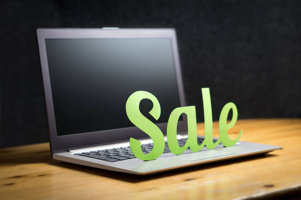 Online store sale campaign ad. Carboard paper letters on laptop. Internet shopping and e-commerce concept. Special offer prices on webshop. Computer on wooden table. Dark and blurred background. - Photo, Image