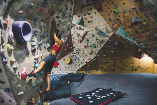 The climber trains on the climbing wall. A woman trains to climb on an artificial relief. A slender girl goes in for sports. - Photo, Image